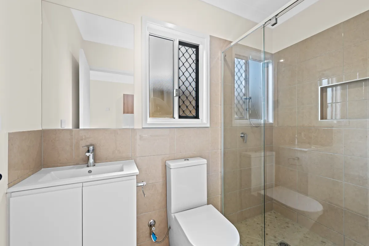 Bathroom in a Brisbane rooming house with a vanity, toilet and glass shower