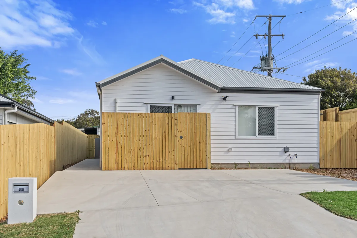 Front of a purpose-built rooming house in Brisbane with white weatherboard cladding, a timber fence and a concrete driveway